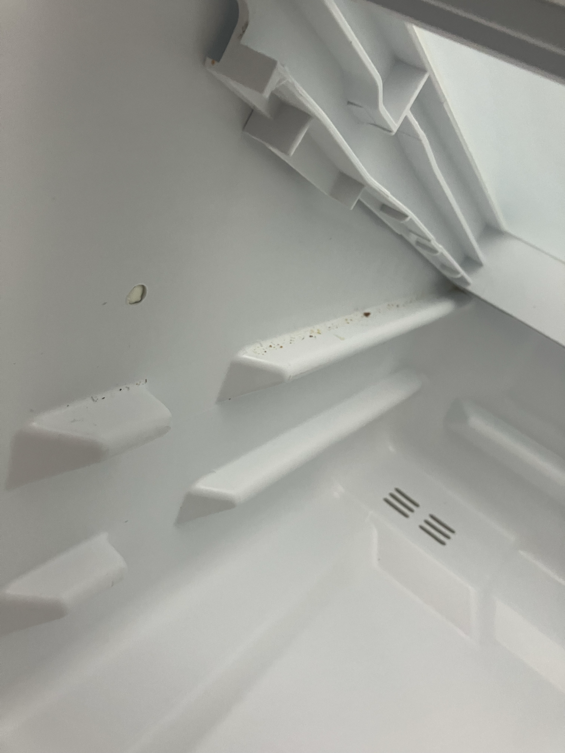 Debris revealed underneath a lifted refrigerator shelf support area